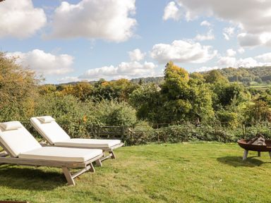 Two padded lounge chairs on a lawn with trees hills and clouds in the background at Rockstowes House Uley near Dursley