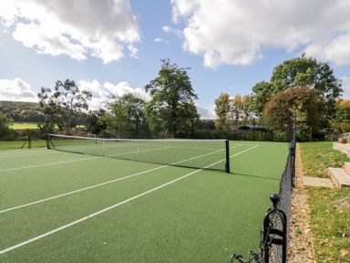 An outdoor tennis court with a net and white lines surrounded by trees at Rockstowes House in Uley near Dursley