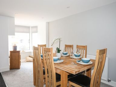 A dining room with a wooden table and six chairs set with plates bowls cutlery and glasses at Bodwena in Moelfre