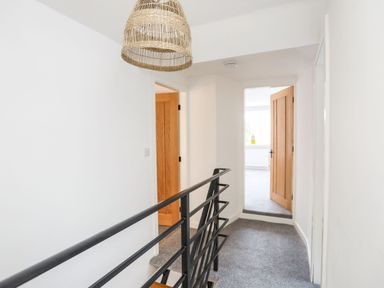A hallway with gray carpet and black metal railing and wooden doors at Bodwena in Moelfre