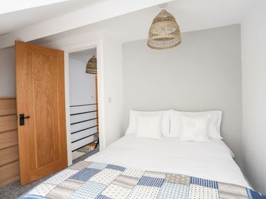 A bedroom with a double bed with white pillows and a patchwork quilt next to a wooden door and a dresser at Bodwena in Moelfre