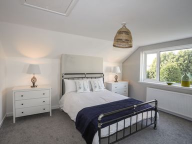 A bedroom with a metal bed frame two white dressers lamps on each dresser and a window with trees outside at Bodwena in Moelfre