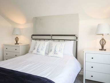 A bedroom with a bed between two white nightstands each with a lamp at Bodwena in Moelfre