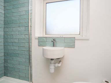 A bathroom with a small white sink below a frosted window and green tiles on the wall at Bodwena Moelfre