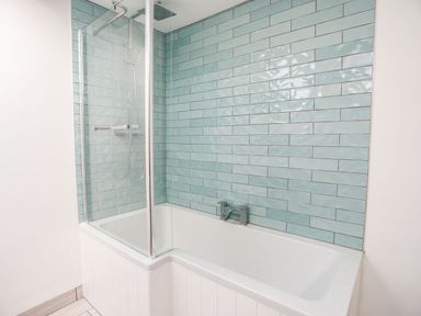 A bathroom with a bathtub and shower area with blue wall tiles at Bodwena in Moelfre