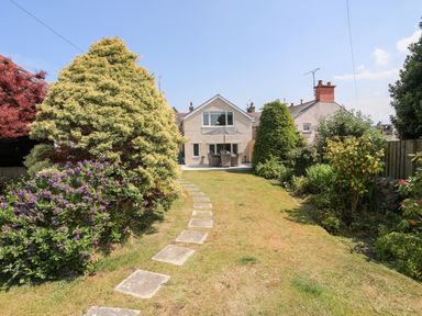 A backyard with a paved pathway leading to a house with a patio and outdoor dining set at Bodwena Moelfre