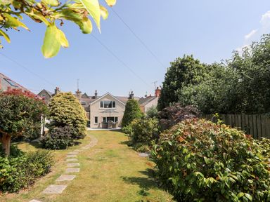 A garden with a stone path leading to a house with patio furniture and an umbrella at Bodwena in Moelfre