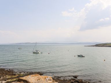 A coastal scene with three boats on the water and rocky shore at Bodwena in Moelfre