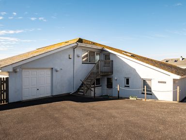 An exterior view of a white house with a sloped roof and outdoor stairs leading to a door at Blue Ridge in Polzeath