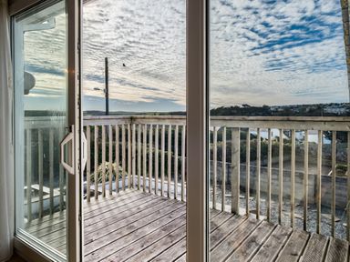 A wooden balcony with railing seen through glass sliding doors at Blue Ridge in Polzeath
