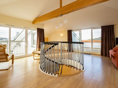 An open living area with a spiral staircase wooden chairs glass doors and brown curtains at Blue Ridge Polzeath
