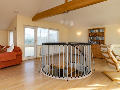 An open room with a spiral staircase railing in the center a red sofa on the left a wooden bookcase filled with books on the right and a white armchair at Blue Ridge Polzeath