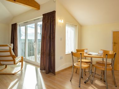 A dining area with a wooden table and four chairs next to a window and glass door with brown curtains at Blue Ridge Polzeath