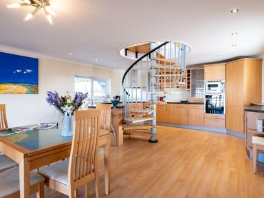 A kitchen and dining area with wooden furniture a spiral staircase and a painting on the wall at Blue Ridge in Polzeath