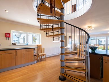 A spiral staircase in a kitchen and dining room with wooden cabinets and a window at Blue Ridge in Polzeath