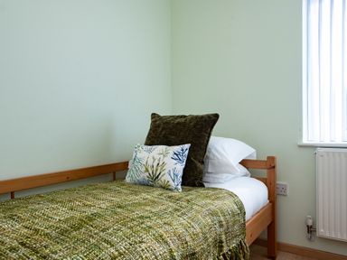 A single bed with green blanket and pillows next to a window with vertical blinds at Blue Ridge in Polzeath