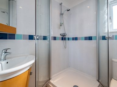 A bathroom shower with glass doors a sink with a faucet and a window at Blue Ridge in Polzeath