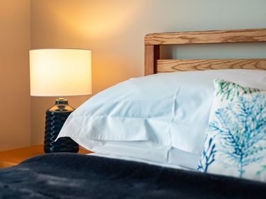 A bedroom with a wooden bed frame white pillows a patterned cushion a bedside table lamp at Blue Ridge in Polzeath
