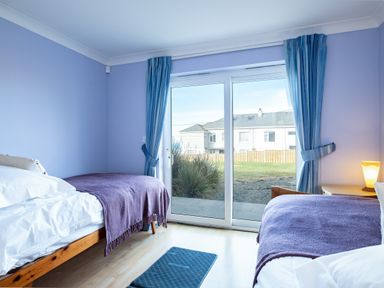 A bedroom with two beds covered with blankets and a sliding glass door with blue curtains at Blue Ridge in Polzeath