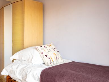 A bedroom with a bed with white pillows and a patterned cushion next to a wooden wardrobe at Blue Ridge in Polzeath