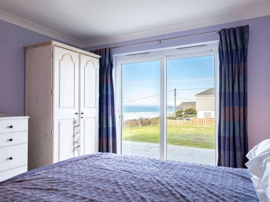 A bedroom with a bed a wardrobe a chest of drawers and sliding glass doors showing an outside view at Blue Ridge in Polzeath
