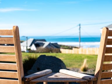 Two wooden chairs facing a distant view of houses a fence and the ocean at Blue Ridge in Polzeath