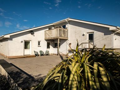 A white building with a balcony three plastic chairs and a patio area with plants at Blue Ridge in Polzeath
