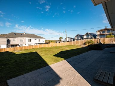 A backyard with a grass lawn and paved patio with surrounding houses behind a wooden fence at Blue Ridge in Polzeath