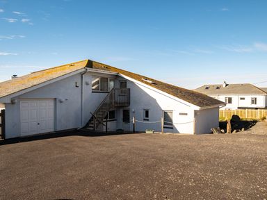 A white building with a sloped roof and exterior stairs next to a paved area at Blue Ridge in Polzeath