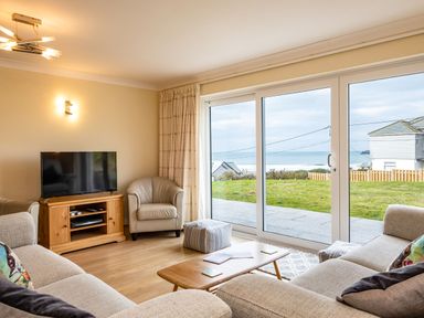 A living room with sofas a wooden TV stand and a large sliding glass door showing a grassy yard and ocean view at Blue Ridge in Polzeath