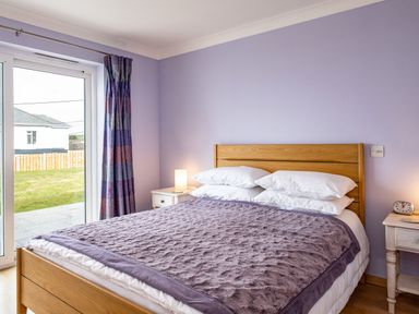 A bedroom with a wooden bed and purple bedding next to a window with curtains at Blue Ridge in Polzeath