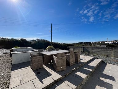 An outdoor patio area with a table and eight wicker chairs and a built-in barbecue at Blue Ridge in Polzeath