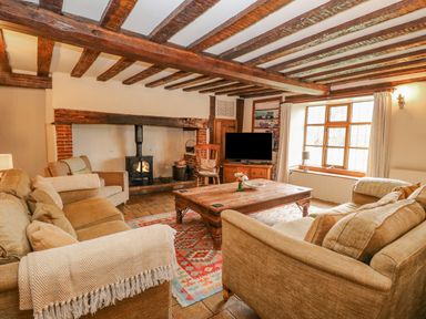 A living room with exposed wooden beams a wood burning stove sofas a wooden coffee table and a television at Manor Farm House in Bacton