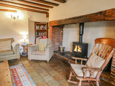A living room with a fireplace an armchair a rocking chair a sofa a wooden coffee table and a bookshelf at Manor Farm House in Bacton