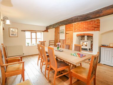 A dining room with a wooden table and chairs a fireplace with wood burning stove and a window at Manor Farm House in Bacton