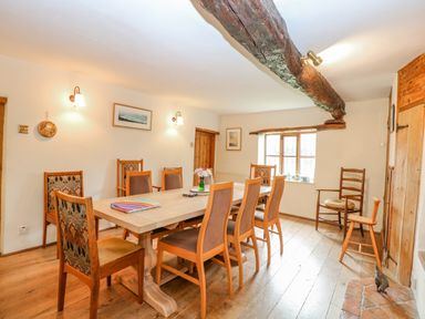 A dining room with a wooden table and chairs wooden beams on the ceiling and a window at Manor Farm House in Bacton