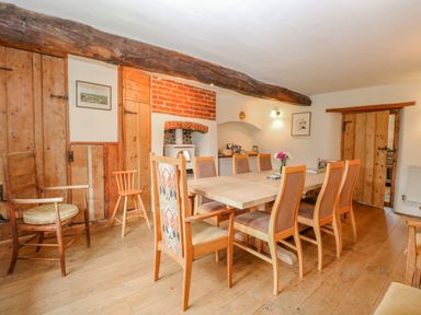 A dining room with wooden table and chairs a wood stove and wooden doors at Manor Farm House in Bacton