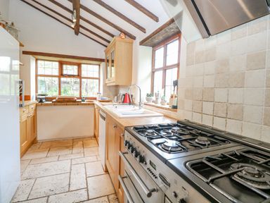 A kitchen with wooden cabinets a gas stove a sink and windows with wooden frames at Manor Farm House in Bacton