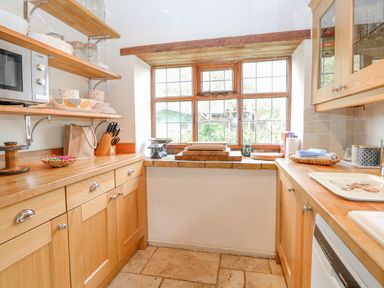 A kitchen with wooden cabinets shelves and a window with a view at Manor Farm House in Bacton