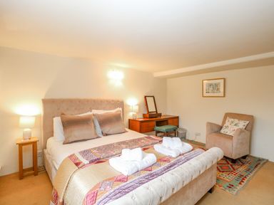 A bedroom with a bed two rolled towels bedside tables a dressing table chair and a rug at Manor Farm House in Bacton