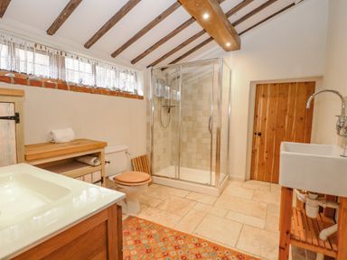 A bathroom with a shower enclosure a toilet a sink wooden ceiling beams and a wooden door at Manor Farm House in Bacton