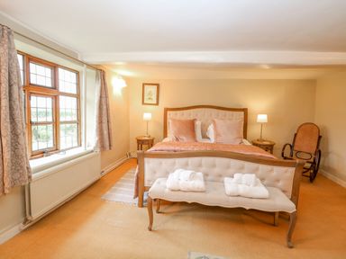 A bedroom with a bed a bench with towels a rocking chair and a window at Manor Farm House in Bacton
