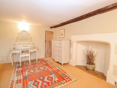 A room with a colorful patterned rug a white dressing table with a chair a white chest of drawers and a plant in a fireplace at Manor Farm House in Bacton