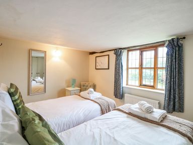 A bedroom with two single beds next to a window with curtains at Manor Farm House in Bacton
