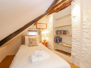 A small bedroom with a single bed white bedding and rolled towels a bookshelf with books and a bedside table with a lamp at Manor Farm House in Bacton