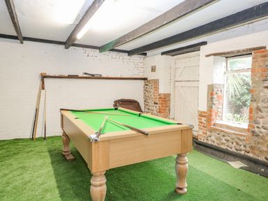 A room with a pool table and pool cues on a green carpet at Manor Farm House in Bacton