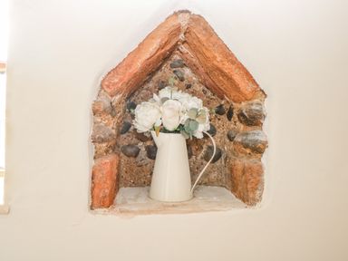 A stone and brick wall niche with a white jug holding white flowers at Manor Farm House in Bacton