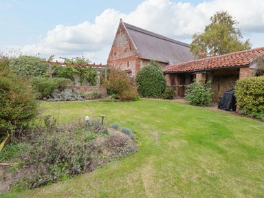 A garden with grass lawn shrubs and a wooden pergola next to brick and tiled roof buildings at Manor Farm House in Bacton