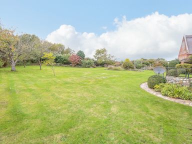 A large grassy garden with trees shrubs and a satellite dish near a brick building at Manor Farm House in Bacton
