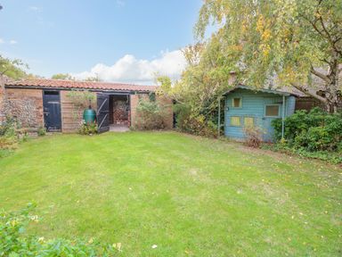 A garden with a brick shed and a blue wooden shed surrounded by trees and bushes at Manor Farm House in Bacton